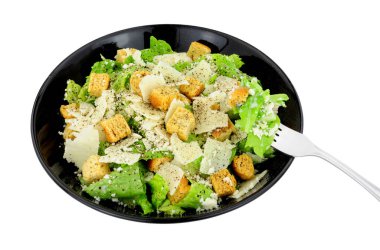 Klasik Sezar salatası, marul ve parmesen peyniri renginde beyaz arka planda izole edilmiş siyah bir tabakta servis ediliyor.