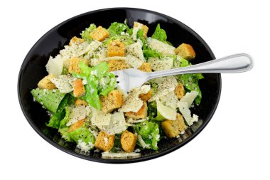 Klasik Sezar salatası, marul ve parmesen peyniri renginde beyaz arka planda izole edilmiş siyah bir tabakta servis ediliyor.