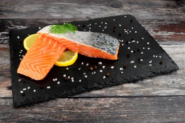 İki taze çiğ somon fileto, dereotlu garnitür ve limon dilimleri servis tahtasında.