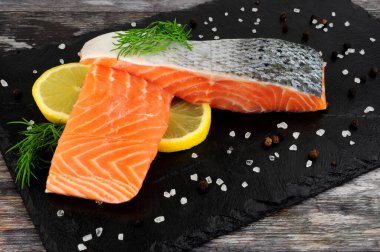 İki taze çiğ somon fileto, dereotlu garnitür ve limon dilimleri servis tahtasında.