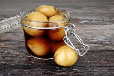 Kırsal ahşap arka planda salamura soğanla dolu cam depolama kavanozu.