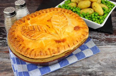 Patates ve bezelye tabağı ile servis edilen hamur işi süslemeli, kıtır hamurlu hamur tatlısı kabında biftek turtası.