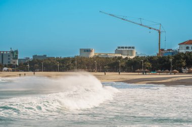 Dalgalar, açık mavi gökyüzü altında kırmızı deniz fenerleriyle Güney Kore 'deki Sokcho İskelesi' ndeki dalgakırana doğru ilerliyor..