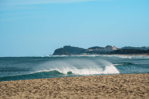 Волны катятся к волнам у причала Сокчо, Южная Корея, с красными маяками под ясным голубым небом.