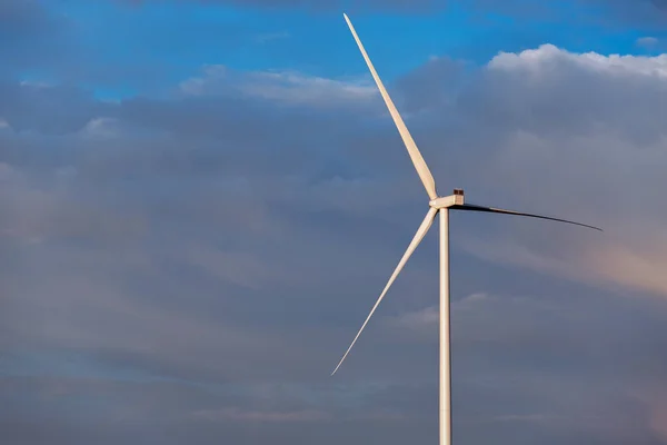 wind turbine offshore windmill of white color made of iron with blades against a blue sky with clouds, alternative electricity preserving nature.