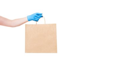 Kahverengi kağıt çevre dostu paket steril eldivenli teslimatçının elini tutuyor beyaz arka plan pankartıyla izole edilmiş kopya alanı, virüs karantina sırasında güvenli teslimat, evde kal.