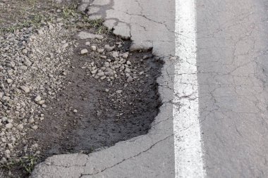 Çürümüş asfalt kaldırımlı, beyaz işaretli yol kenarında çukur, yolda tehlike, kimse yok..