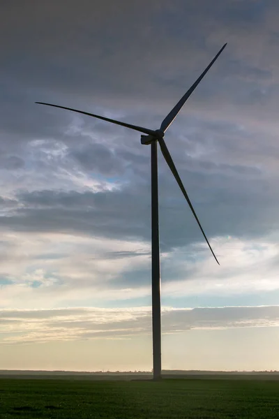 silhouette wind turbine offshore windmill made of iron with blades on field against a blue sky with clouds on sunset, alternative electricity preserving nature.