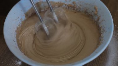 Hamuru hazırlamak bir mikserle çırpmak evde ahşap bir masada tatlı hamur işleri pişirmek..