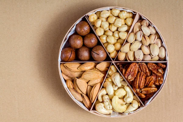 木制圆形礼品盘 带有三角细胞 混合不同类型的坚果 供素食主义者在纸生态工艺背景下健康饮食 — 图库照片