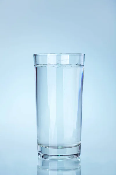 clear glass beaker filled with water with a reflection on a cold blue background a water utensil item, nobody.