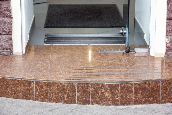 granite threshold from stone tiles store entrance with glass door and rug with foot mat closeup, nobody.