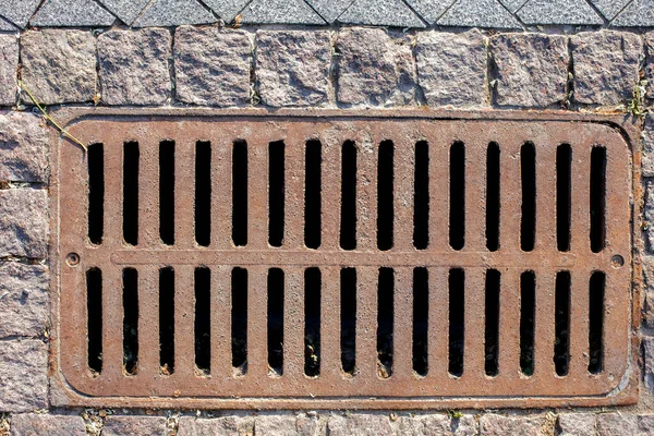 ラフカットの石のタイルの上から歩道の排水システムの錆びたマンホールの長方形の格子 — ストック写真