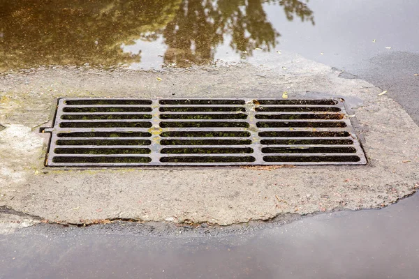 雨の後の水溜りで道路上の雨水を排水するためのハッチグレートを有する不完全な排水システム誰も — ストック写真