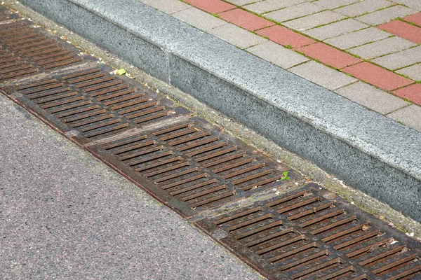 道路表面からの雨水排水のための排水システムの格子の長方形のハッチ道路脇の石瓦の歩道で縁部にアスファルトの道路と — ストック写真