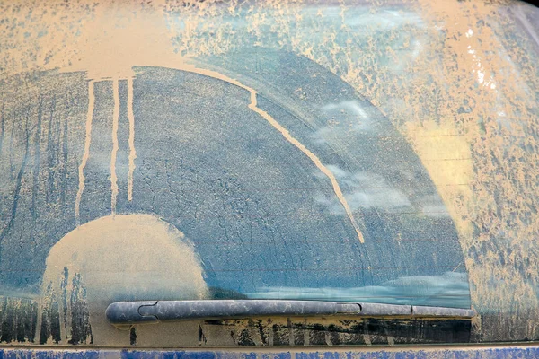 dirty heated rear window covered with a layer of dust with a wiper blade swipe close-up, dirty blue car.