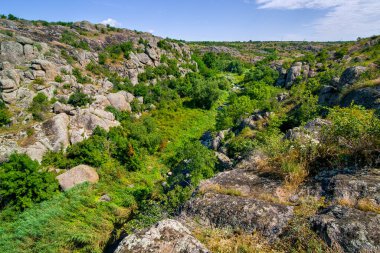 Güneşli bir yaz gününde uçurumun tepesinde granit kayalar bulunan kanyonun doğal manzarası, bir dağ nehri ve aşağıdaki vadide sazlıklar, hiç kimse.