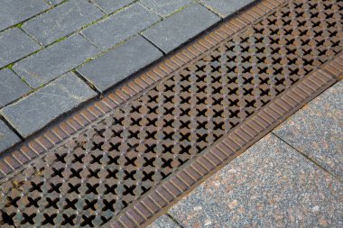 Granit kiremitlerden yapılmış kaldırımda demir desenli bir kafes ile kaplanmış bir drenaj hendeği. Asfaltlı bir yolun yağmur drenaj sistemine yakın çekim taşları..