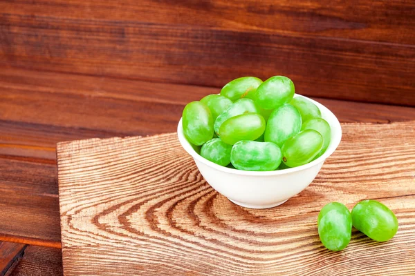 White grapes in a drinking bowl on a wooden table.