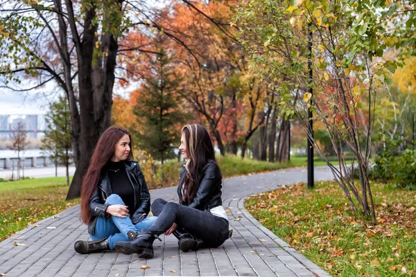 Две Молодые Женщины Осенью Парке Сидят Тропинке Фоне Деревьев Желтыми — стоковое фото