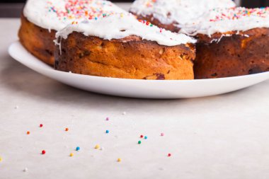 Ev mutfağında beyaz bir tabakta taze hamur işleri. Beyaz kremayla süslenmiş çörekler ve masaya saçılmış renkli konfetiler serpiştirilmiş..