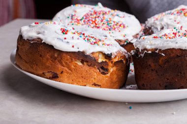 Ev mutfağındaki bir tabakta taze pişmiş hamur işlerinin yakın çekimleri, beyaz bir katmanın altında kuru üzümlü, çırpılmış yumurta beyazı, renkli konfeti ile süslenmiş..