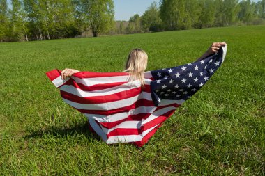 Amerika Birleşik Devletleri bayrağına sarılı yeşil çimlerin üzerinde oturan bir Rus kadının dikiz aynasıyla yaprak döken bir huş ağaçlarının karşısındaki görüntüsü..