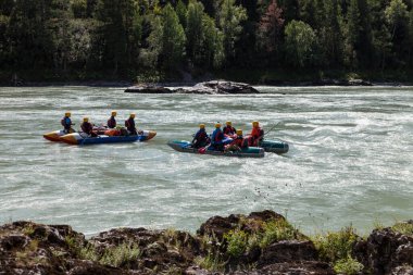 Ekipman, can yelekleri ve sarı miğferler içinde rafting yapan bir grup insan dağ nehri boyunca yükselen küreklerle birlikte mavi şişme bir teknede..
