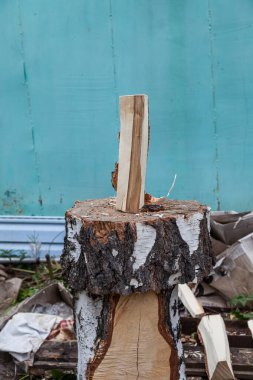 Güvertede bir baltayla ikiye bölünmüş bir kütük, erkek eli kumaş eldivenli ve arka bahçede kamuflaj ceketli. Kışa hazırlanmak için ev işi..
