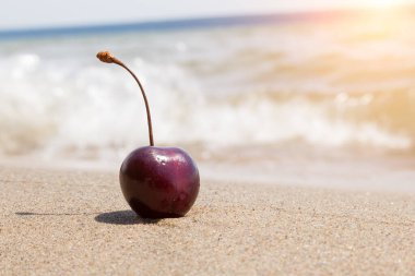 Kumsalda kumsalda olgun kırmızı kirazlar, güneşli bir günde dalgaların arka planına karşı romantik baştan çıkarıcı bir tatlı..