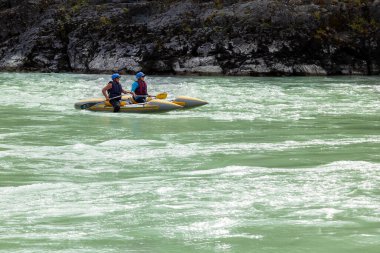 Novosibirsk, Rusya - 08.14.2020: Turuncu can yeleği giymiş bir grup insan, dağ nehri boyunca uzanan mavi ve sarı renkli lastik botlarla orman arka planına karşı rafting yapıyorlar