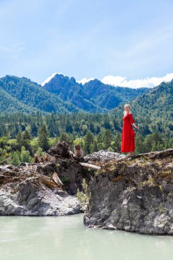 Kırmızı elbiseli sarışın kadın, Katun nehrinin kıyısındaki kaya taşlarının üzerinde duruyor. Yazın dağların arka planına atlamadan önce kollarını yana açıyor. Göt herif. İntihara meyilli.