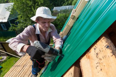 İnşaat işçileri yeni çatı, çatı döşeme araçları, yeni çatılarda metal levhalarla kullanılan elektrikli matkaplar kuruyor. Emekli bir adamın kendi yaptığı bir ev..