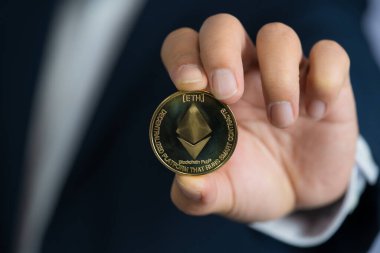 Altın Ethereum ETH 'de dahil olmak üzere kripto para birimi de mavi takım elbiseli bir adamın elinde. Dosyaladım, verdim, verdim..