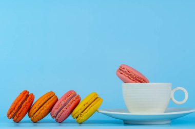 Makaron ya da badem kurabiyesi tatlıları ve renkli Fransız tatlıları mavi arkaplanda ve boş alanda izole edilmiş kahve fincanının üzerinde bulunan klasik renk ya da pastel renktir..