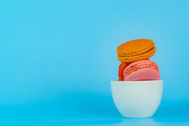 Makaron ya da badem kurabiyesi tatlıları ve renkli Fransız tatlıları mavi arkaplanda ve boş alanda izole edilmiş kahve fincanının üzerinde bulunan klasik renk ya da pastel renktir..