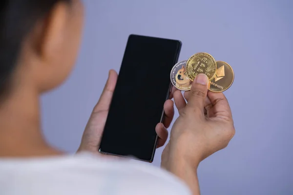 Altın Bitcoin Dogecoin DOGE, Ethereum ETH grubu ele geçirilmiş kadın ya da kız üzerinde Cryptocurrency ve cep telefonu akıllı telefonu ile birlikte dosyalandı ve mor arka plan verildi. alışveriş çevrimiçi kavramı.