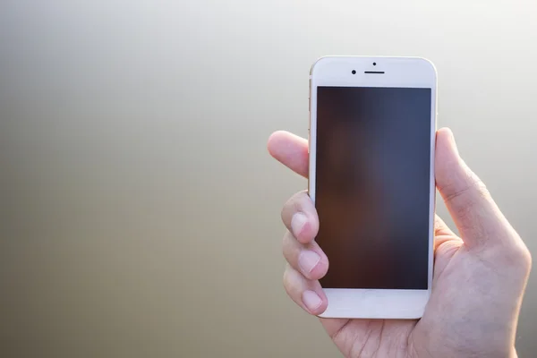 Man hand met smartphone tegen op gladde achtergrond. — Stockfoto