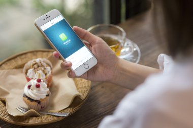 CHIANG MAI, THAILAND - JUNE 28, 2015: Woman hold iPhone 6 with social Internet service WhatsApp on the screen in coffee shop. iPhone 6 was created and developed by the Apple inc.