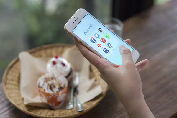 CHIANG MAI, TAILANDIA - 28 de junio de 2015: Todos los iconos populares de las redes sociales en la pantalla del dispositivo inteligente Apple iPhone 6 en la mano de la mujer en la cafetería . —  Fotos de Stock