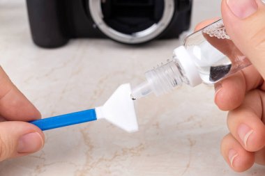 Kameraya bir damla sensör temizleyicisi sürüyorum ve lensleri çıkarıyorum. Rutin toz temizliği ve fotoğraf malzemelerindeki lekeler. Bakım ekibi yakın plan. Ön görünüm.