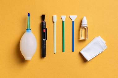 Hava üfleyici, lens kalem, üç farklı bez, sıvı sensör temizleyici ve sarı arka planda mikrofiber. Fotoğraf teçhizatı bakımı için temizlik seti. Üst görünüm. 