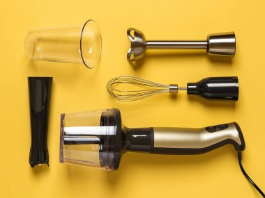 Sarı zemin üzerine eklenmiş farklı eklentiler ve fincanlar ile daldırma el blenderi. Sos, smoothie ve püre yapmak için modern elektrikli mutfak gereçleri. El karıştırıcı seti. Düz yatıyordu.