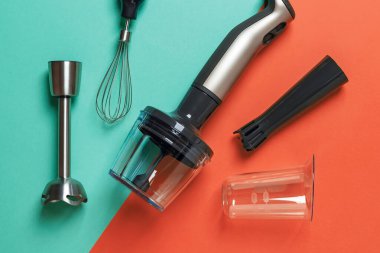 Yeşil arka planda farklı eklentiler ve bardaklarla daldırma el blenderi. Sos, smoothie ve püre yapmak için modern elektrikli mutfak gereçleri. El karıştırıcı seti. Üst görünüm.