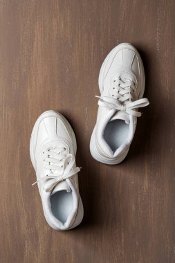 Kahverengi arka planda bir çift beyaz bağcıklı spor ayakkabı. Aktif yaşam tarzı, spor ve spor için yeni unisex topaklı ayakkabılar. Uzayı kopyala Üst görünüm.