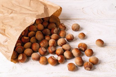 Soyulmamış fındıklar bir kese kağıdından beyaz ahşap masaya döküldü. Fındık, ketojenik diyet ve vejetaryenlik için antioksidan ve protein kaynağıdır. Üst görünüm.