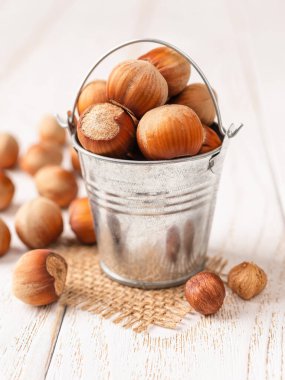 Beyaz ahşap masanın üzerinde küçük metal bir kovada fındık. Sağlıklı vejetaryen yiyecekler, antioksidan ve protein kaynağı. Ketojenik ve çiğ gıda diyetleri. Hasat konsepti. Ön görünüm.