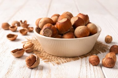 Beyaz ahşap bir masada bej bir seramik kasede kabuksuz fındık. Sağlıklı vejetaryen yiyecekler, antioksidan ve protein kaynağı. Ketojenik ve çiğ gıda diyeti malzemesi. Ön görünüm.