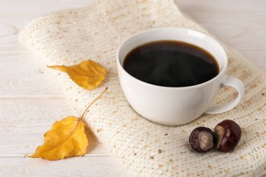 Bej örgü bir eşarp ve beyaz ahşap kırsal yüzey üzerinde iki sarı yaprak üzerinde büyük beyaz buharda pişmiş kahve kupası. Sıcak sonbahar konsepti. Ön görünüm. 