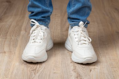 Ayakları beyaz dantelli topaklı ayakkabı ve kahverengi zeminde mavi kot pantolon içinde duruyordu. Aktif yaşam tarzı, günlük yaşam ve spor için bir çift yeni rahat ayakkabı. Düşük açı görünümü. 